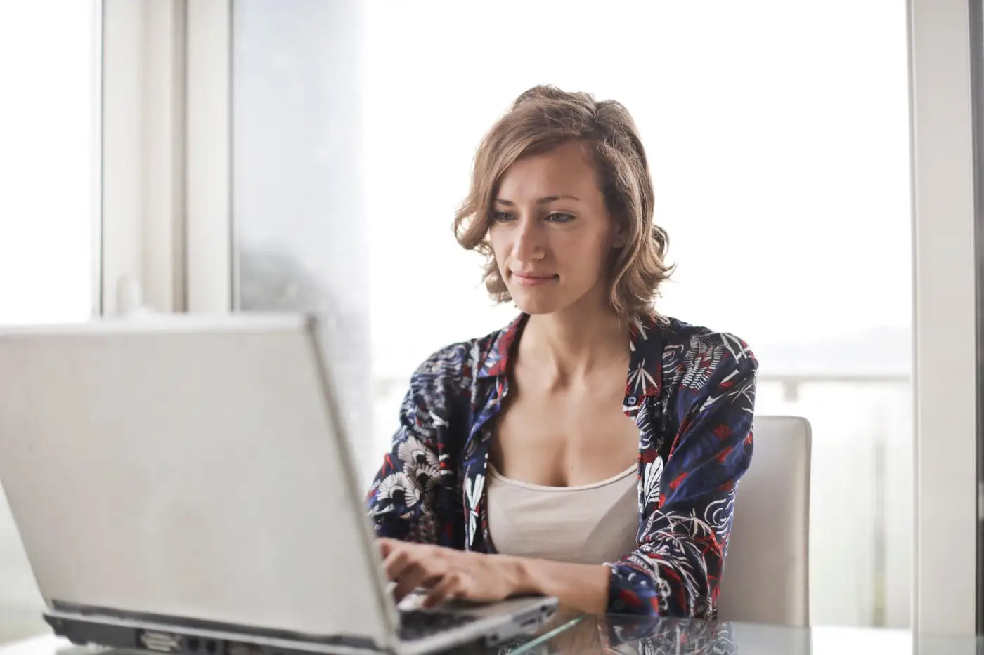 Woman working thoughtfully at a laptop by a bright window