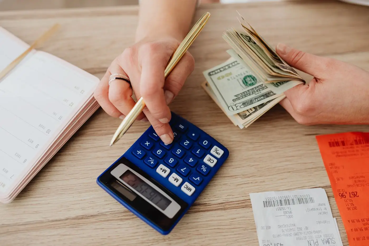 Hands holding banknotes and a pencil over a blue calculator, notebook and receipts