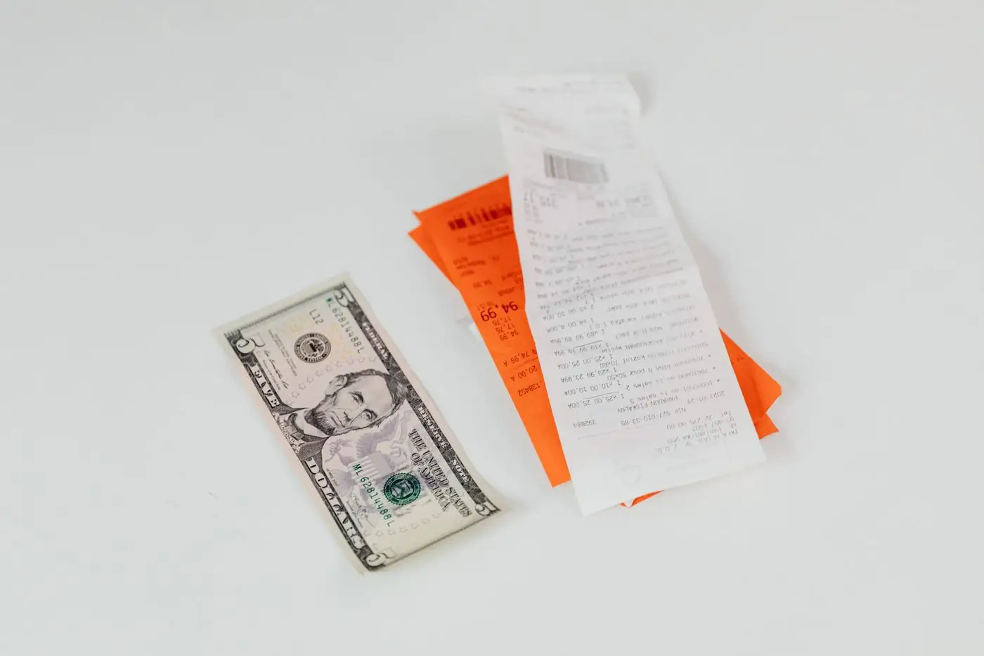 A five-dollar bill beside folded receipts on a white table