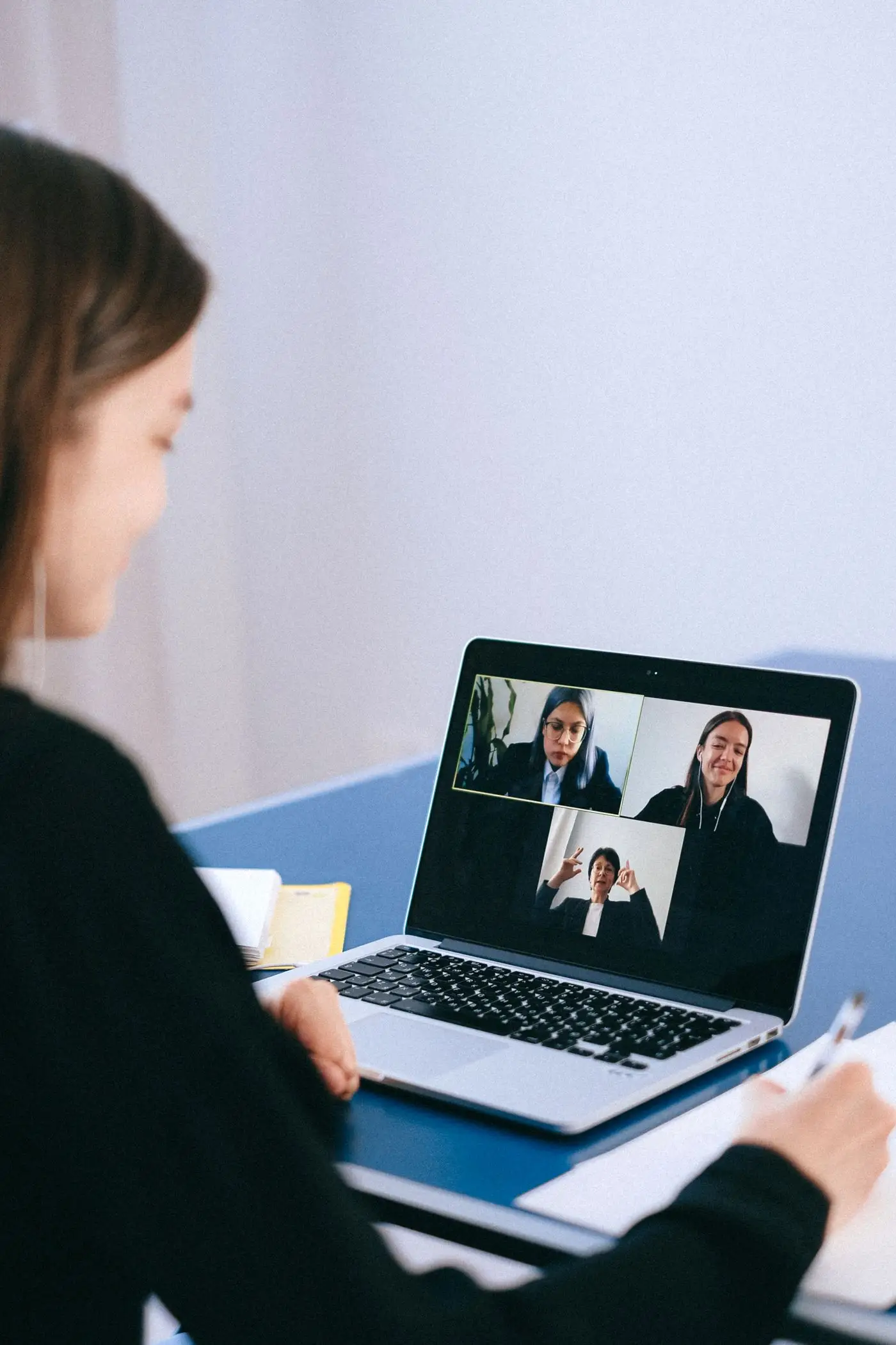 Woman on a video call with a coach, taking notes at her desk