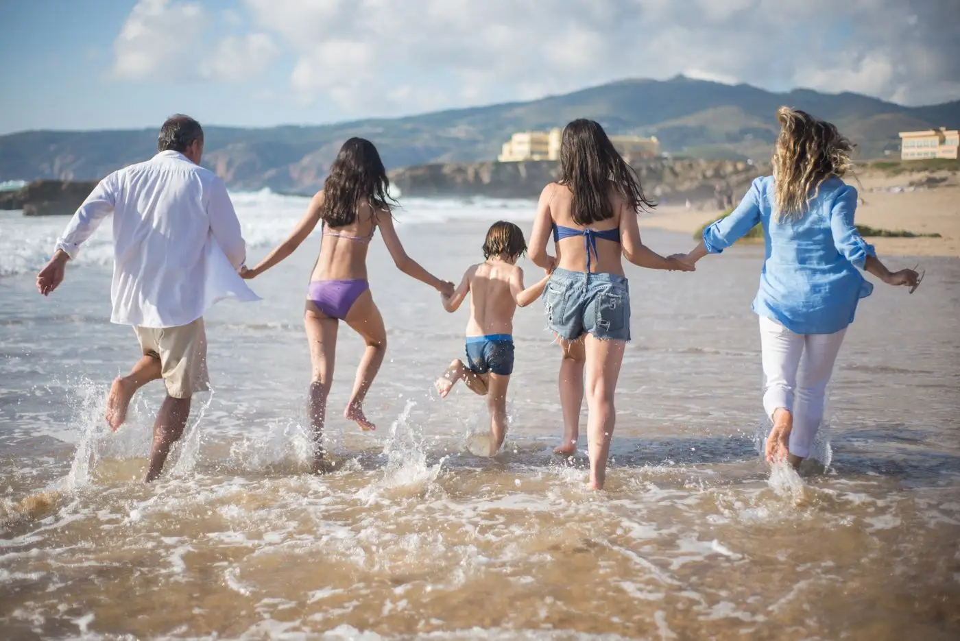 Family running into the sea together on a sunny beach holiday