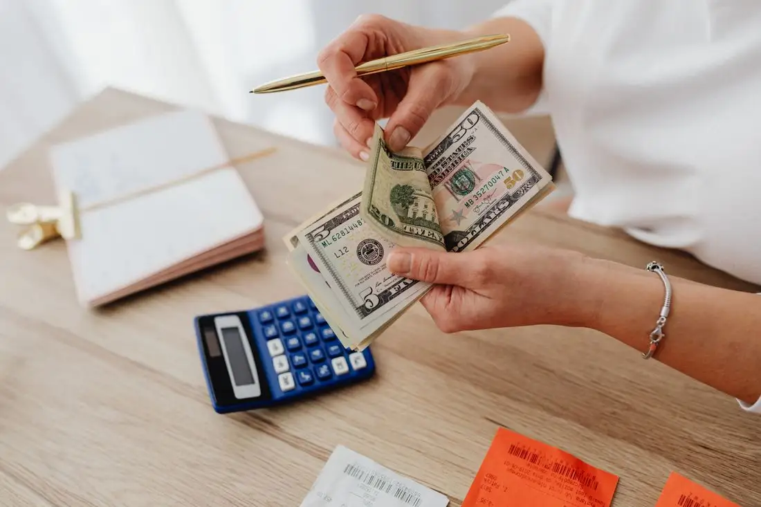 Hands counting cash beside a calculator and an open notebook while planning monthly spending