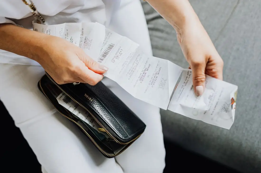 Person sorting paper receipts into piles next to an open wallet during a spending review