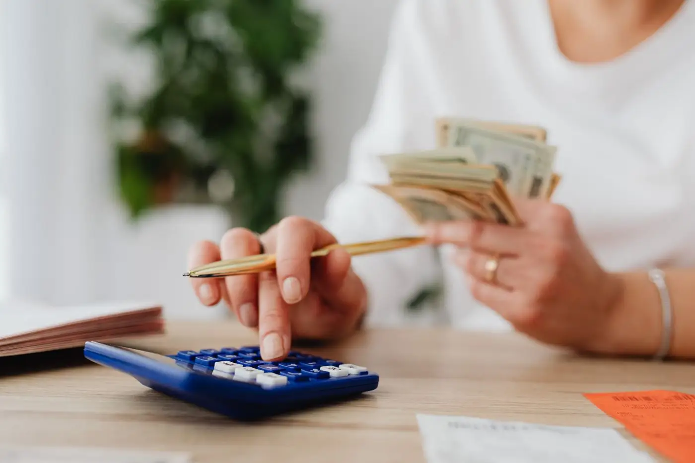 Hands holding cash and a pencil above a calculator and notebook