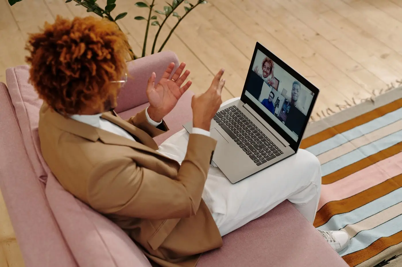 Woman on a pink sofa talking with her coach on a laptop video call