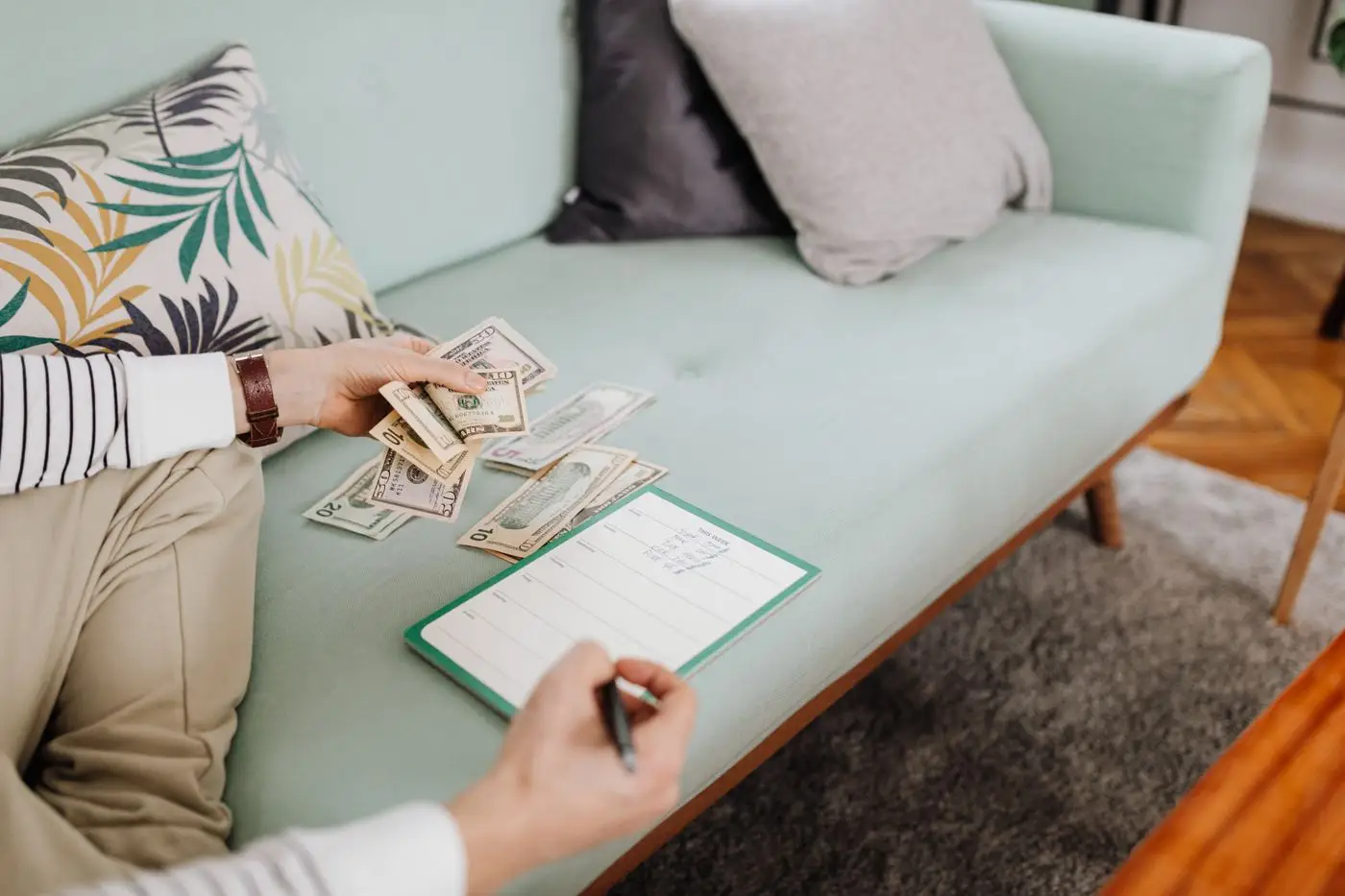 Couple on a mint sofa counting cash and writing in a notebook together