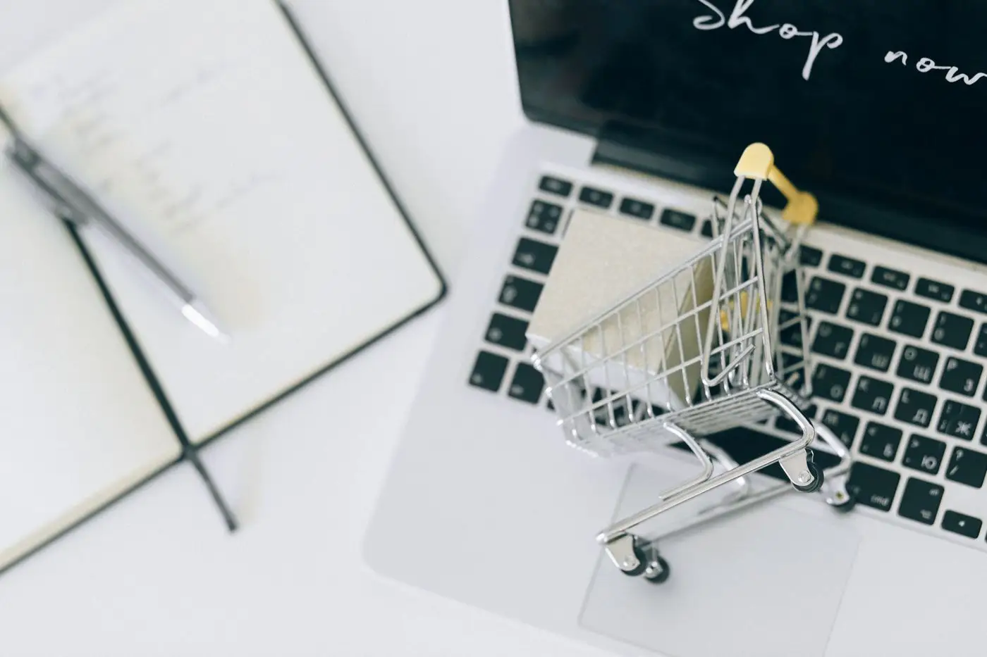 Laptop showing an online shop with a tiny shopping cart on the keyboard