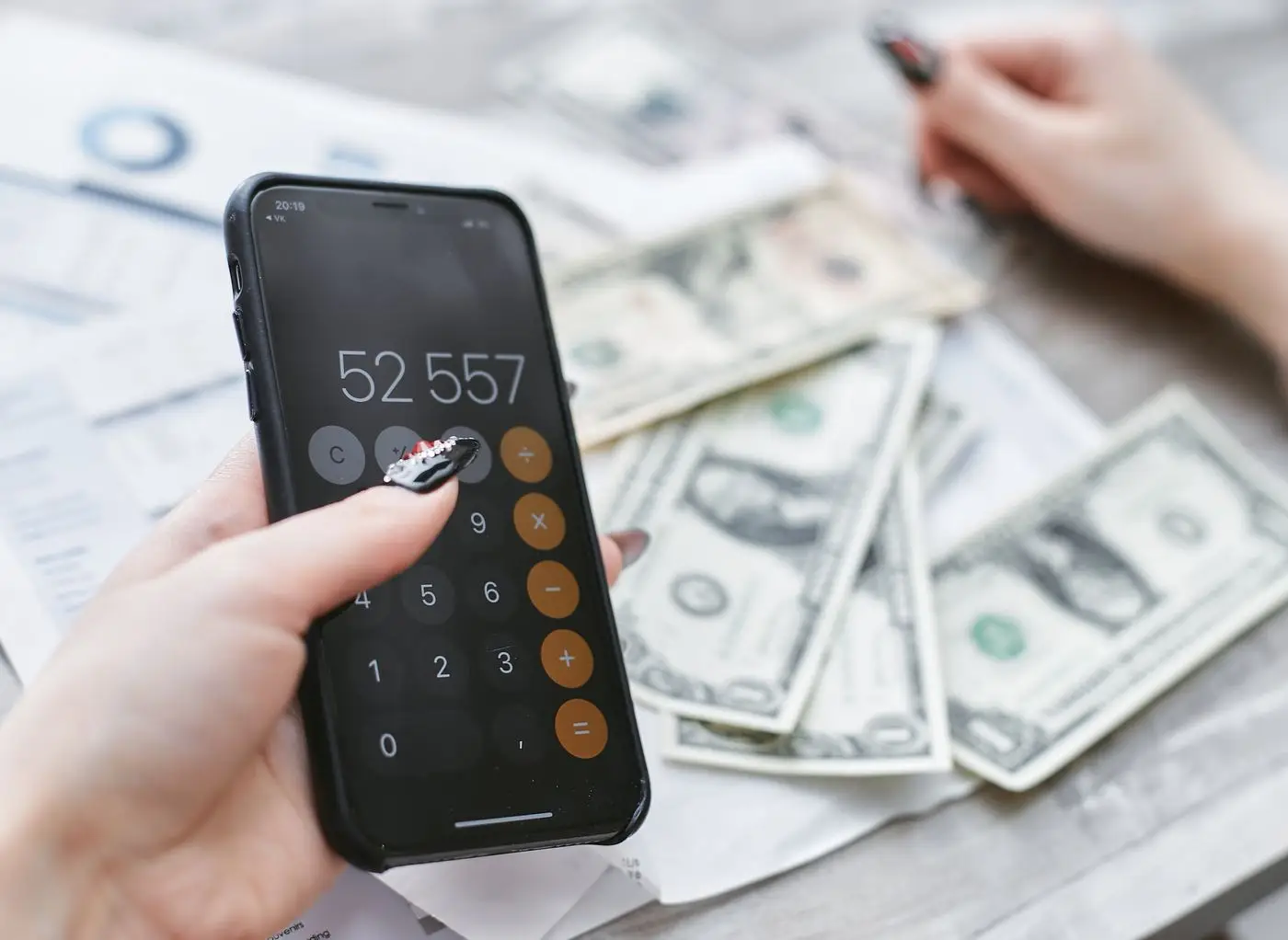 Hand holding a phone calculator above a spread of dollar bills